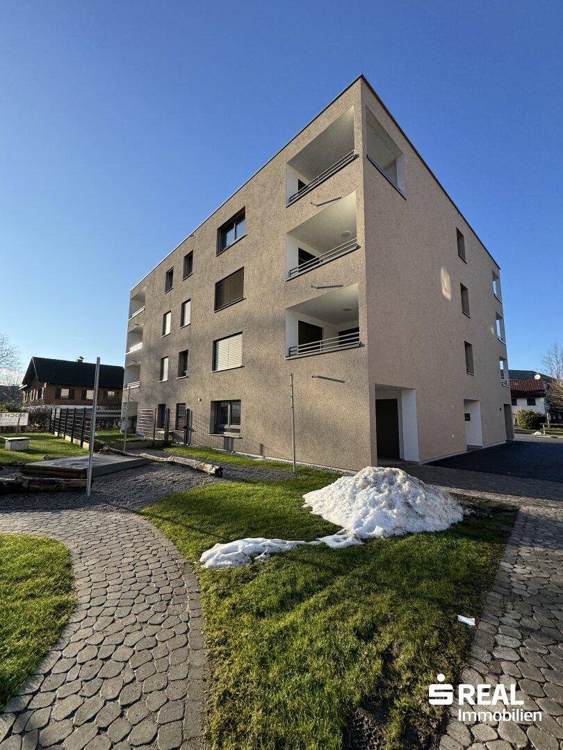 Modernes Mehrfamilienhaus mit beiger Fassade, mehreren Balkonen und gepflegter Außenanlage.