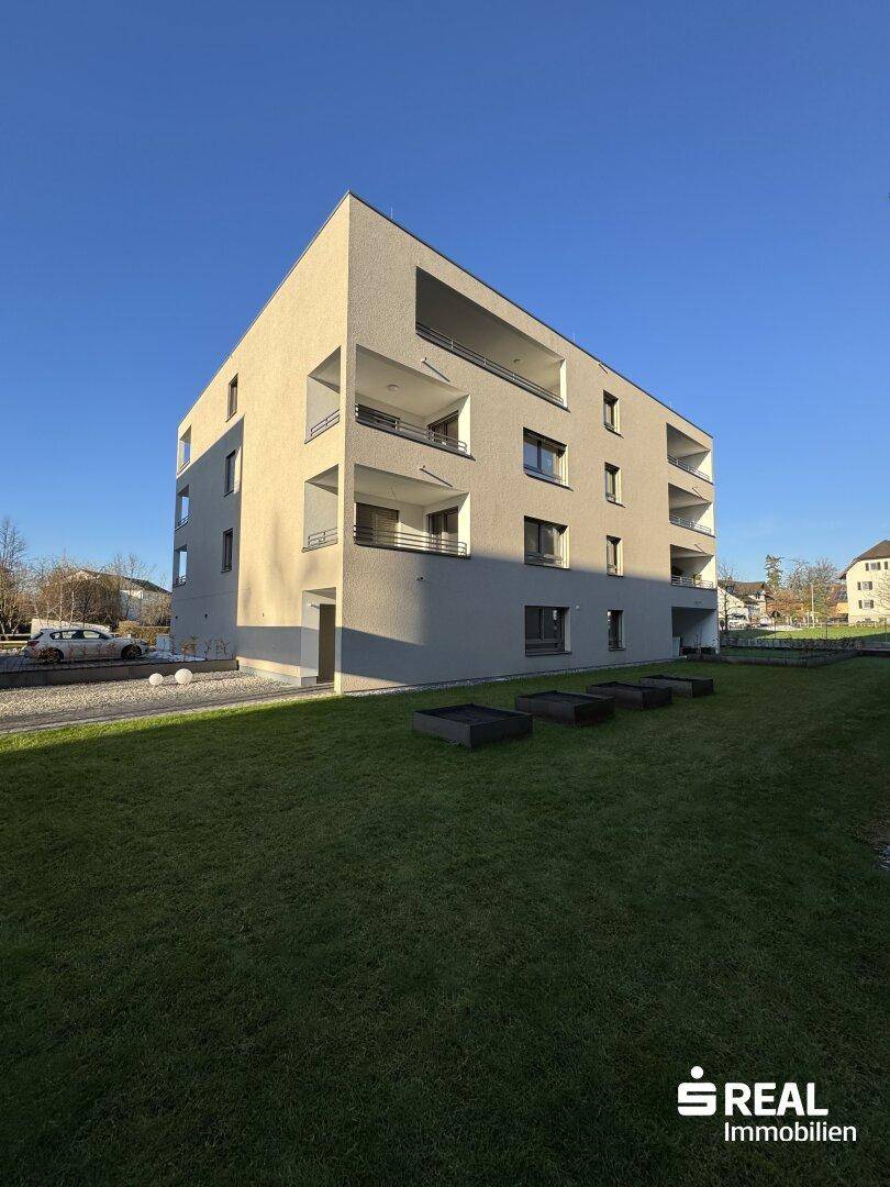 Modernes Mehrfamilienhaus mit klarer Architektur, Balkonen und gepflegter Grünfläche.