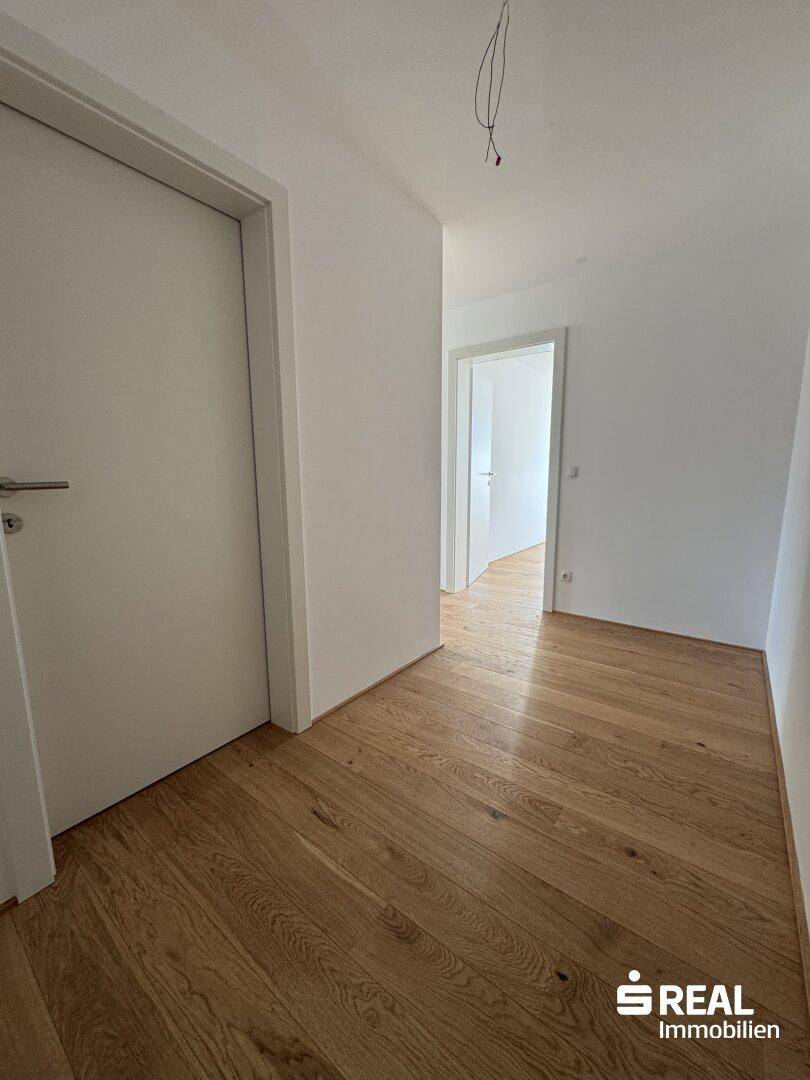 Geräumiger Flur mit elegantem Holzfußboden und weißen Türen, der zu weiteren Räumen führt.