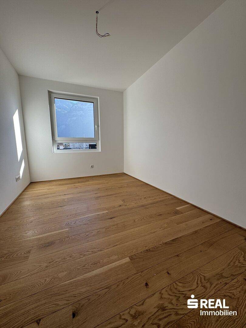 Helles Schlafzimmer mit hochwertigem Holzparkett und einem großen Fenster für viel Tageslicht.