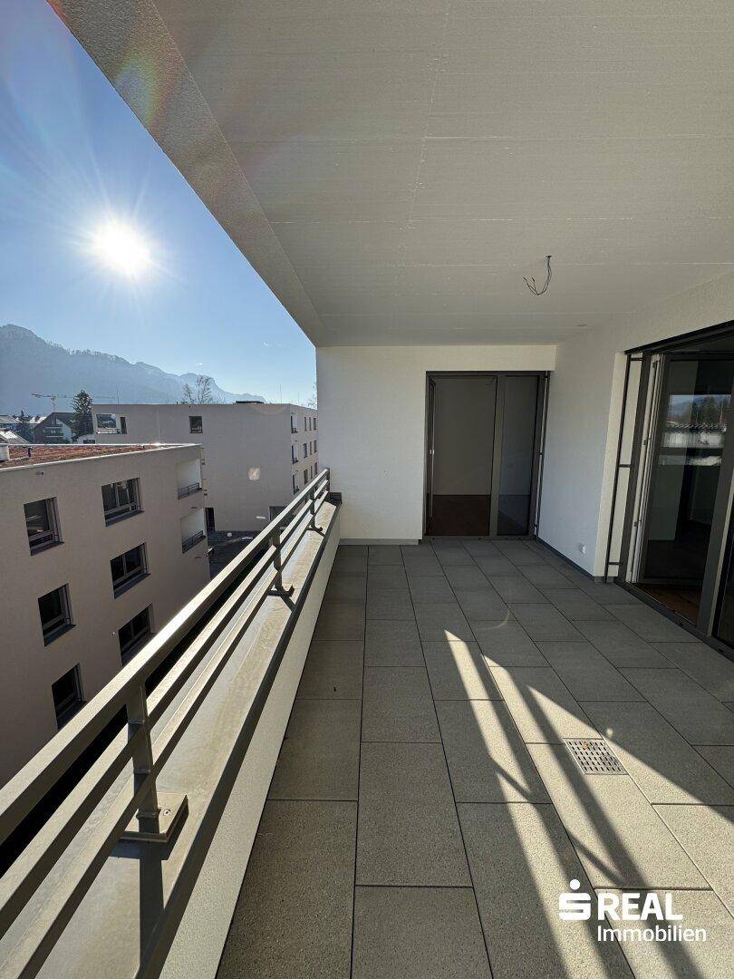 Sonniger Balkon mit Fliesenboden und Blick auf die umliegenden Gebäude und die Berglandschaft.