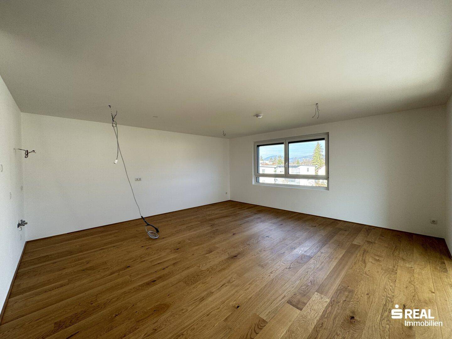 Leeres Zimmer mit hellem Holzfußboden und einem Fenster, bereit für die individuelle Gestaltung.