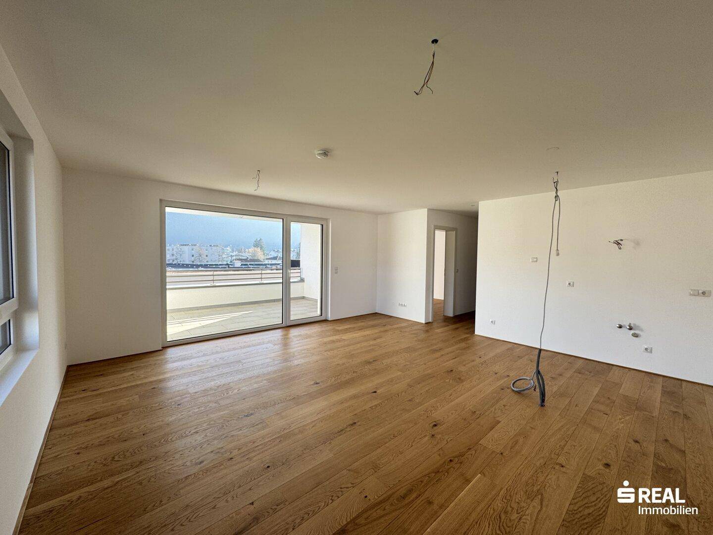 Heller, leerer Wohnraum mit Echtholzparkett und großem Schiebefenster zum Balkon.