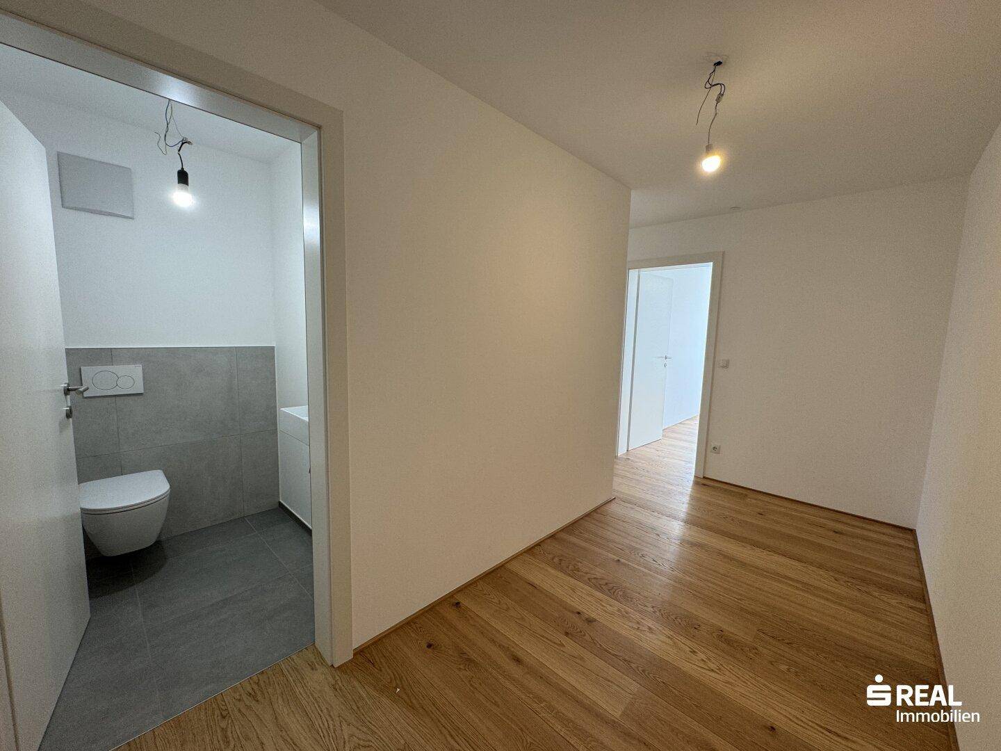 Heller Flur mit hochwertigem Holzparkett, der zu den verschiedenen Zimmern und dem Gäste-WC führt.