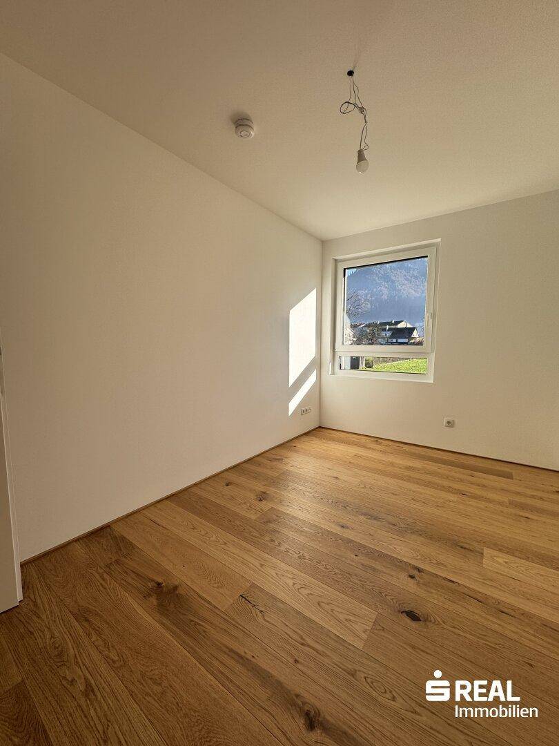 Sonniges Zimmer mit hellem Holzparkett und einem Fenster mit Ausblick auf die umliegende Bergwelt.