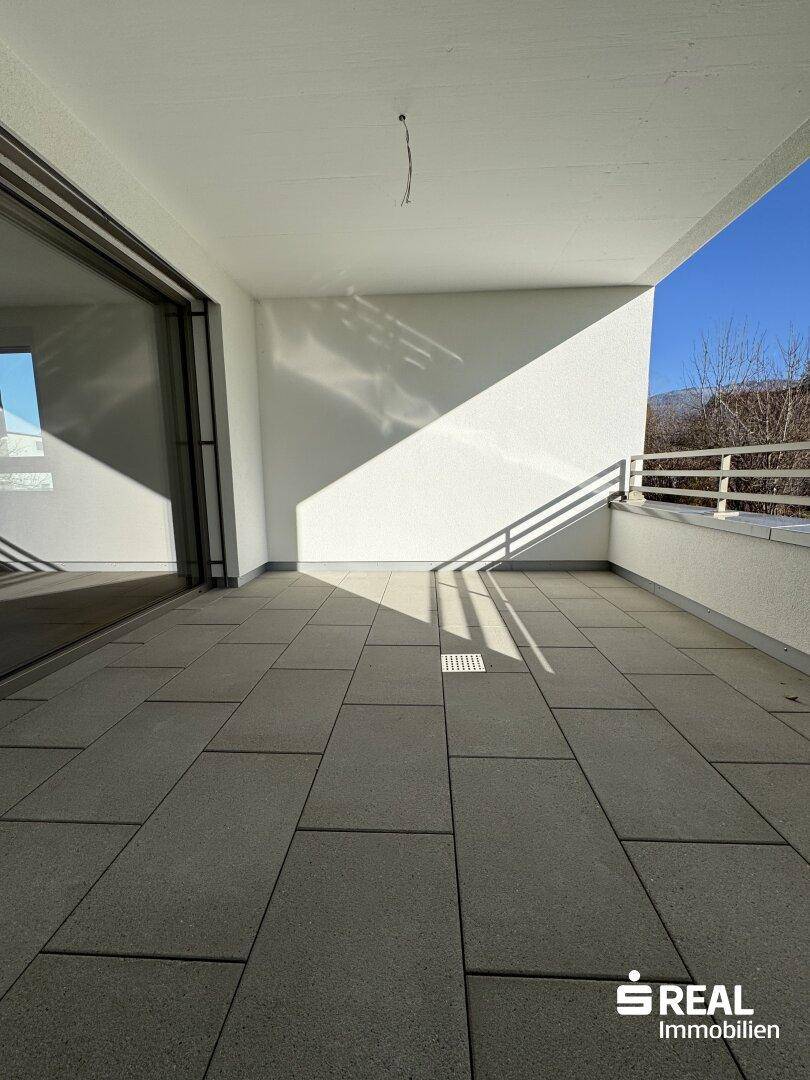Sonniger Balkon mit modernen Fliesen und einem weiten Blick auf Bäume und die Berglandschaft.