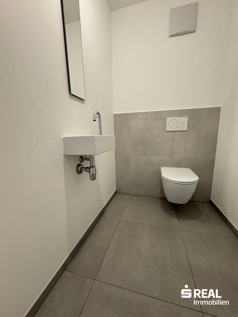 Kleines Gäste-WC mit modernen grauen Fliesen, wandhängendem WC und minimalistischem Waschbecken.