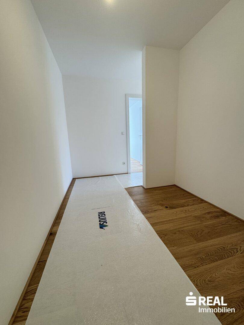 Heller Flur mit neuem Holzparkettboden und weißen Wänden, teilweise durch Schutzfolie abgedeckt.