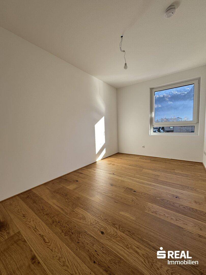 Helles Schlafzimmer mit neuem Holzparkettboden und einem Fenster, das viel Tageslicht hereinlässt.
