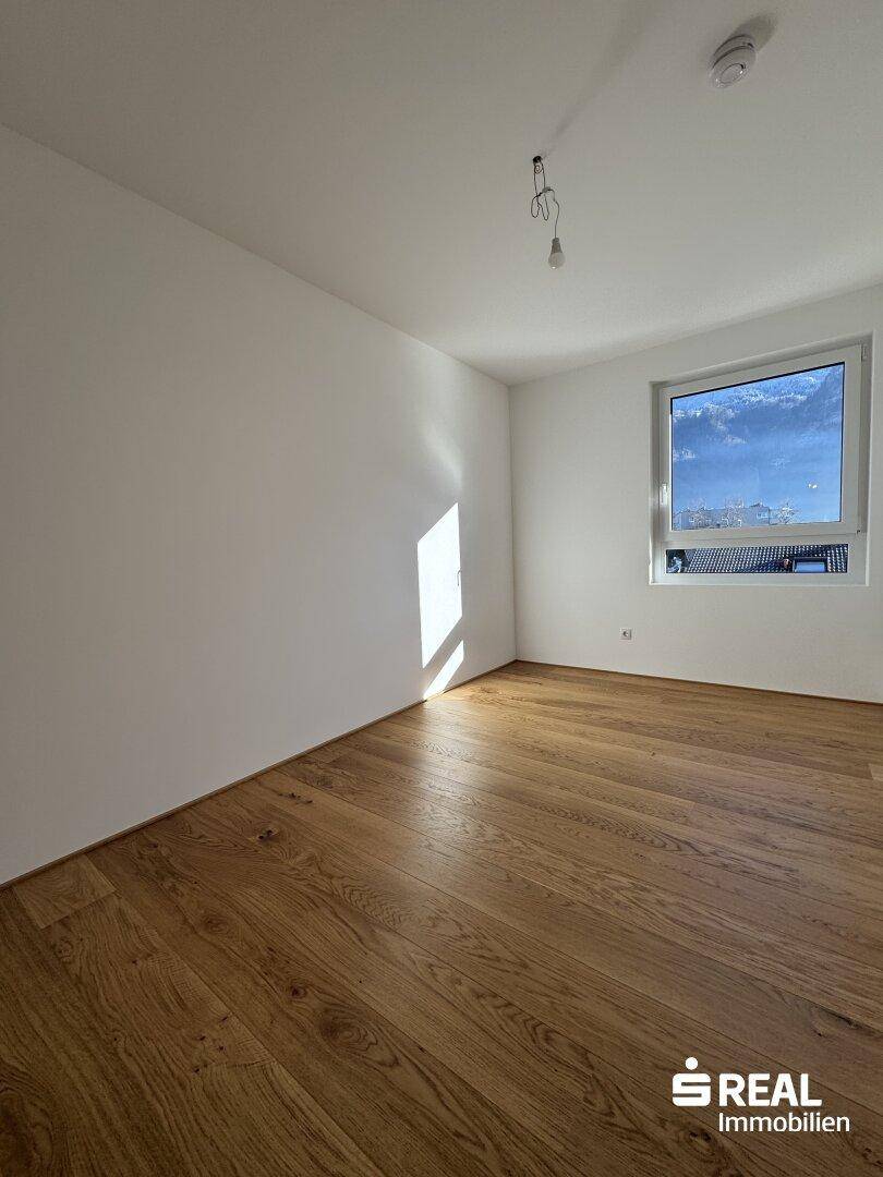 Geräumiges Schlafzimmer mit hellem Holzparkett und einem großen Fenster für optimale Belichtung.