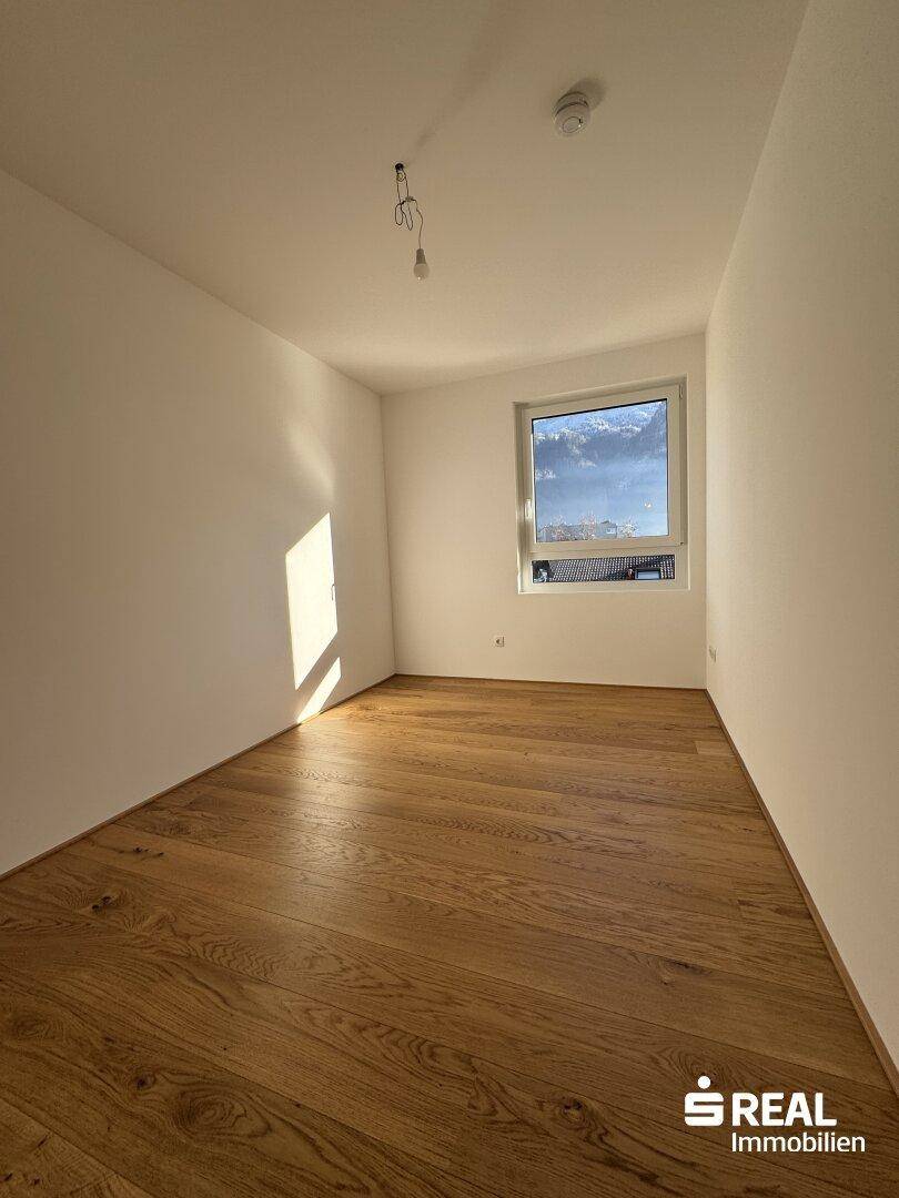 Lichtdurchflutetes Zimmer mit hochwertigem Holzparkett und einem Fenster mit Blick nach draußen.