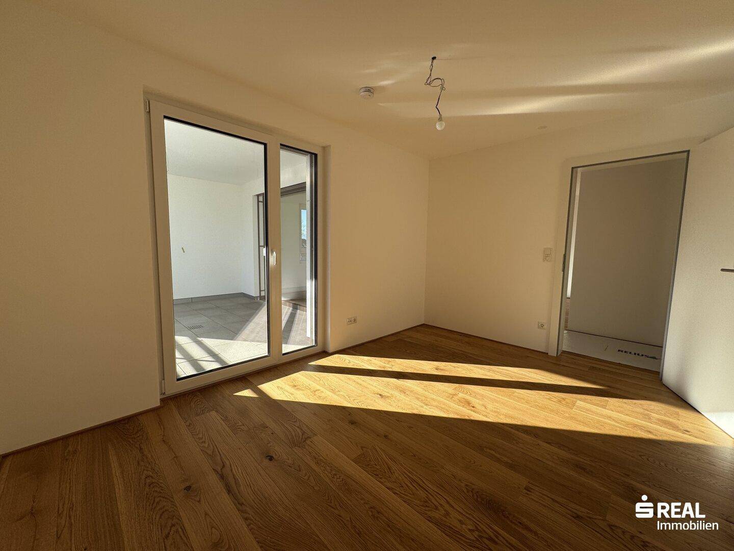 Geräumiges Wohnzimmer mit Holzparkett und Zugang zu einem Balkon oder einer Terrasse, sehr hell.