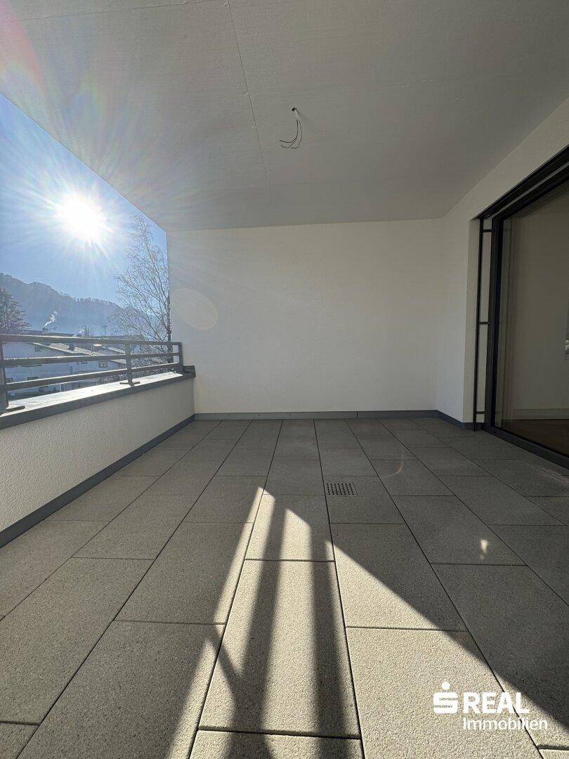 Großer, sonniger Balkon mit modernen grauen Fliesen und Metallgeländer, ideal zum Entspannen.
