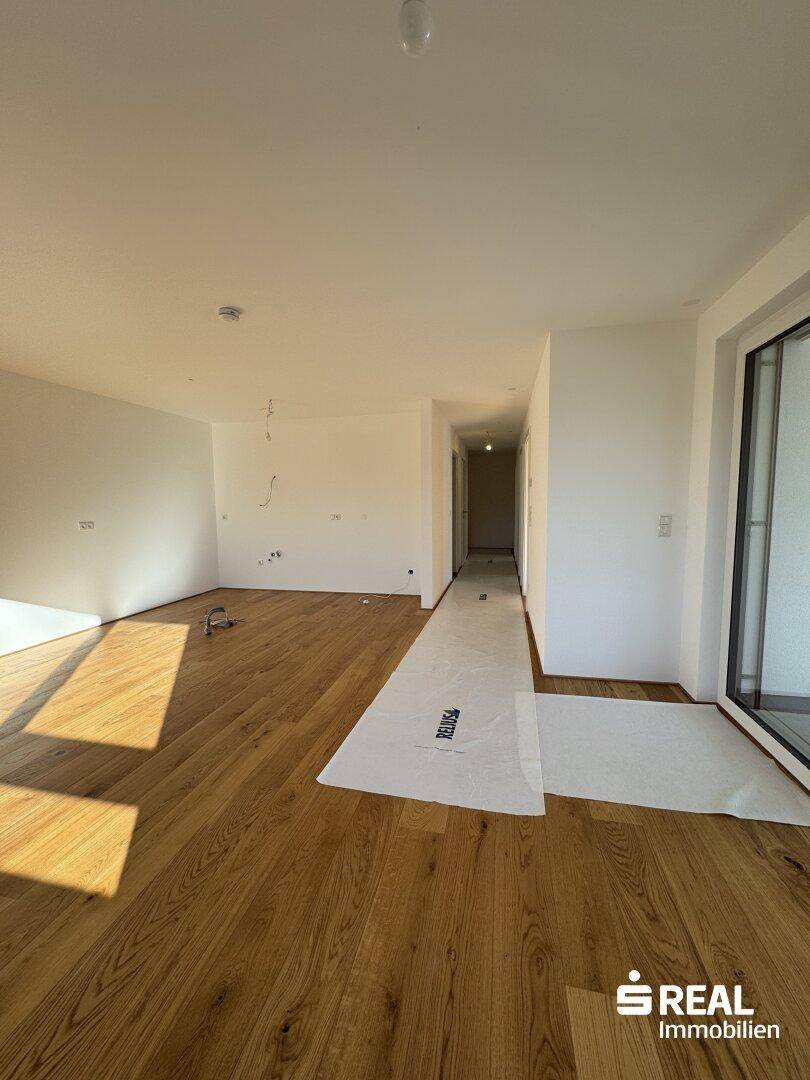 Großer, heller Wohnbereich mit Holzparkettboden und Zugang zu einem sonnigen Außenbereich.