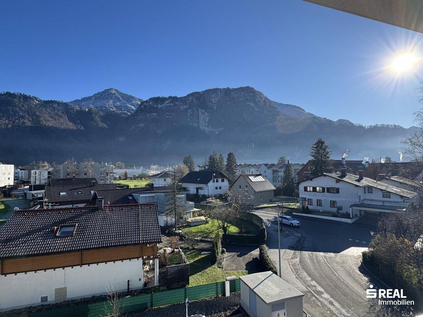 Weitläufiger Blick über eine Wohnsiedlung mit majestätischen Bergen im Hintergrund an einem sonnigen Tag.