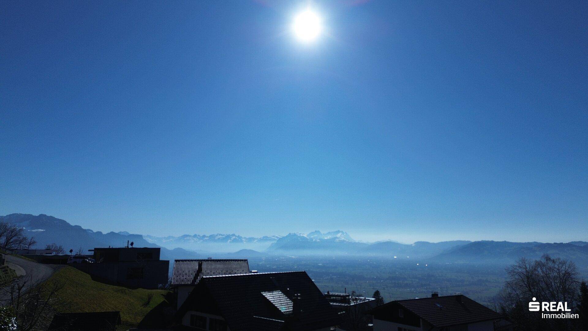 Sonniger Panoramablick über eine Siedlung mit Bergen und weitem Horizont im Hintergrund.