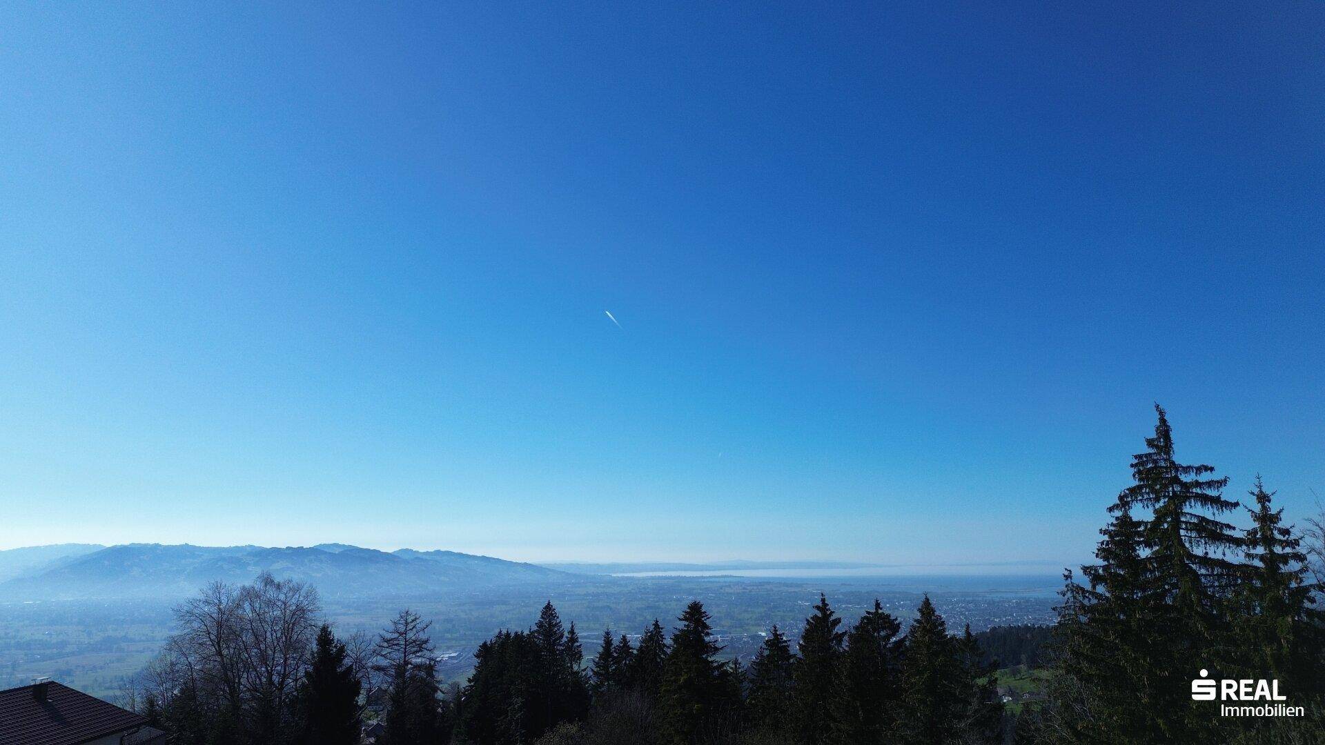 Klarer blauer Himmel über einer weiten Landschaft mit nebelverhangenen Bergen am Horizont.