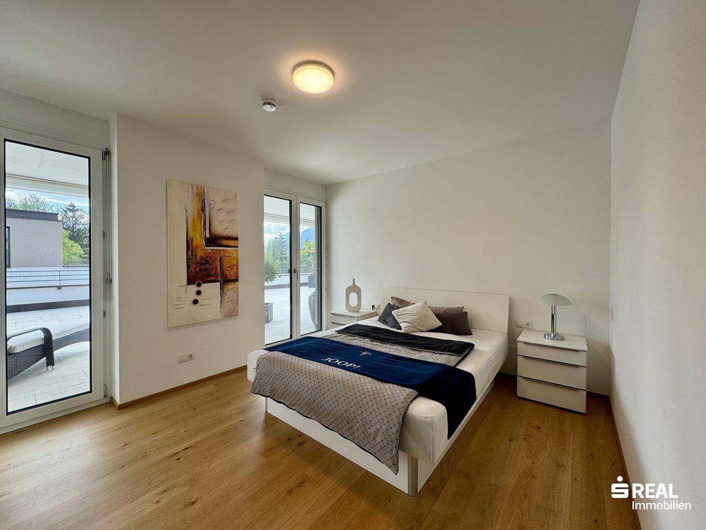 Helles Schlafzimmer mit Holzboden, Doppelbett und Zugang zur großen Dachterrasse.