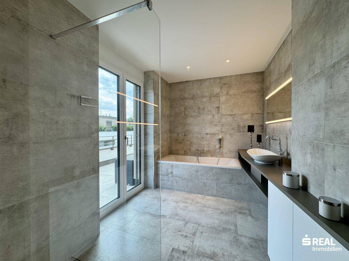 Modernes Badezimmer mit großer Badewanne, begehbarer Dusche und Zugang zur Terrasse.