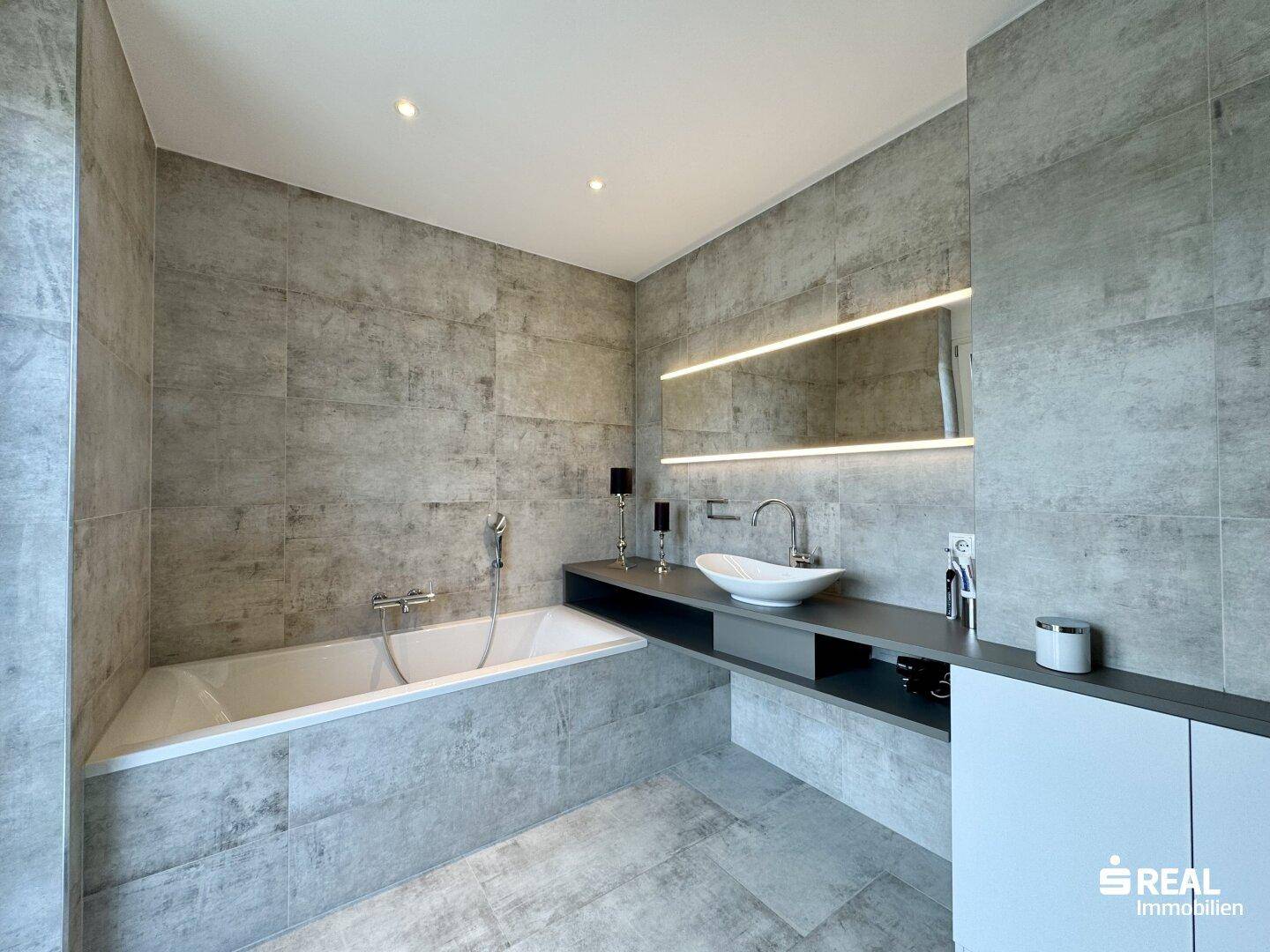 Modernes Badezimmer mit grauen Fliesen, Badewanne und stilvollem Aufsatzwaschbecken.