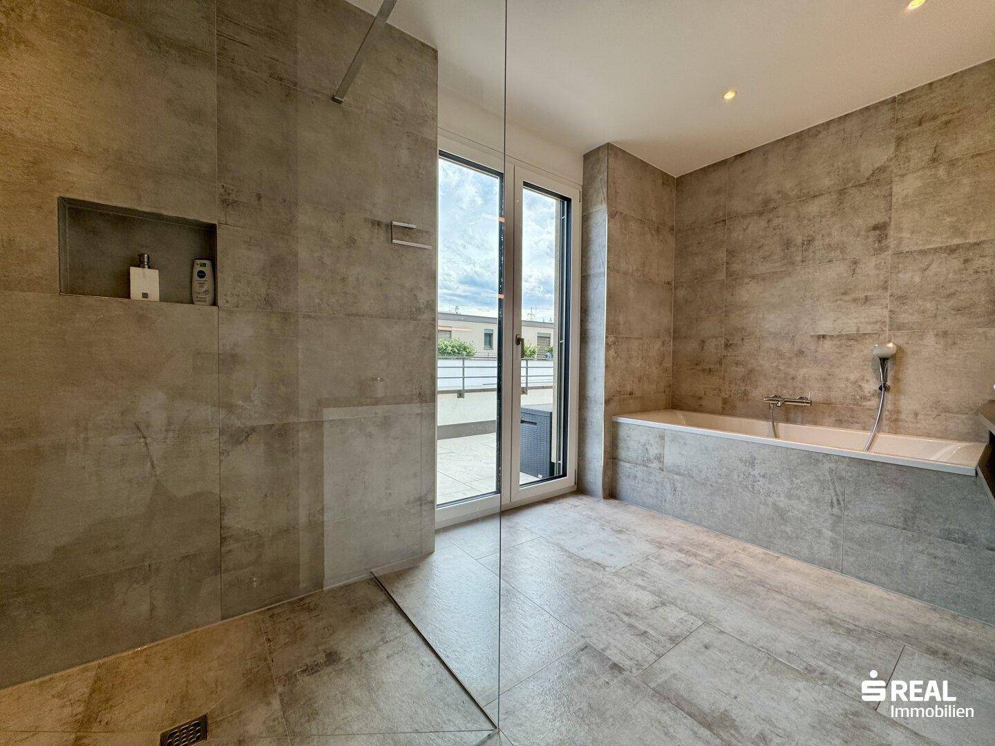Elegantes Badezimmer mit Badewanne, begehbarer Dusche und großen Fenstern zur Terrasse.