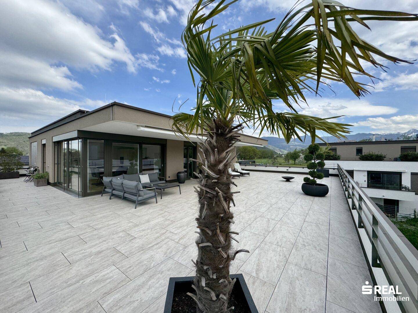 Weitläufige Dachterrasse mit Palmen, Liegestühlen und Panoramablick auf die Berge.