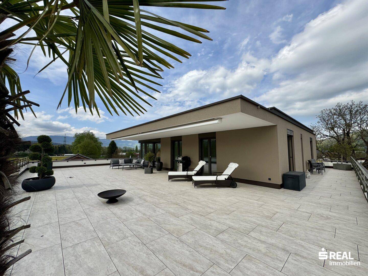 Große, sonnige Dachterrasse mit modernen Loungemöbeln, Liegestühlen und weitem Blick in die Landschaft.