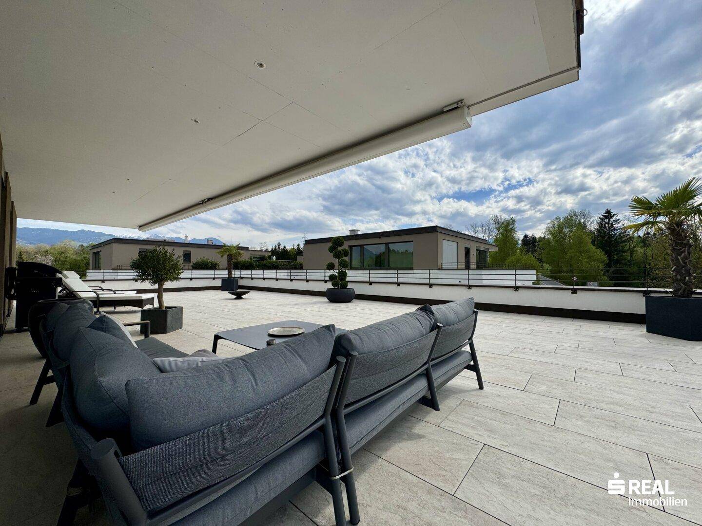 Große Dachterrasse mit bequemen Loungemöbeln unter einer Markise und weitem Ausblick.