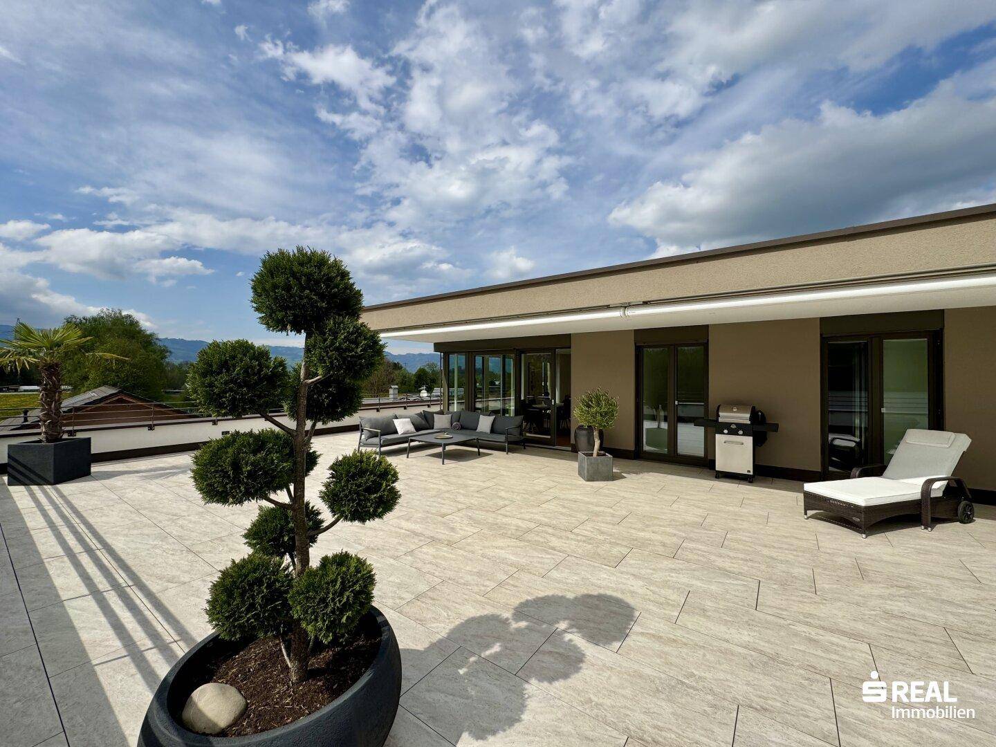Weitläufige Dachterrasse mit dekorativen Pflanzen, Loungemöbeln und Grillbereich.