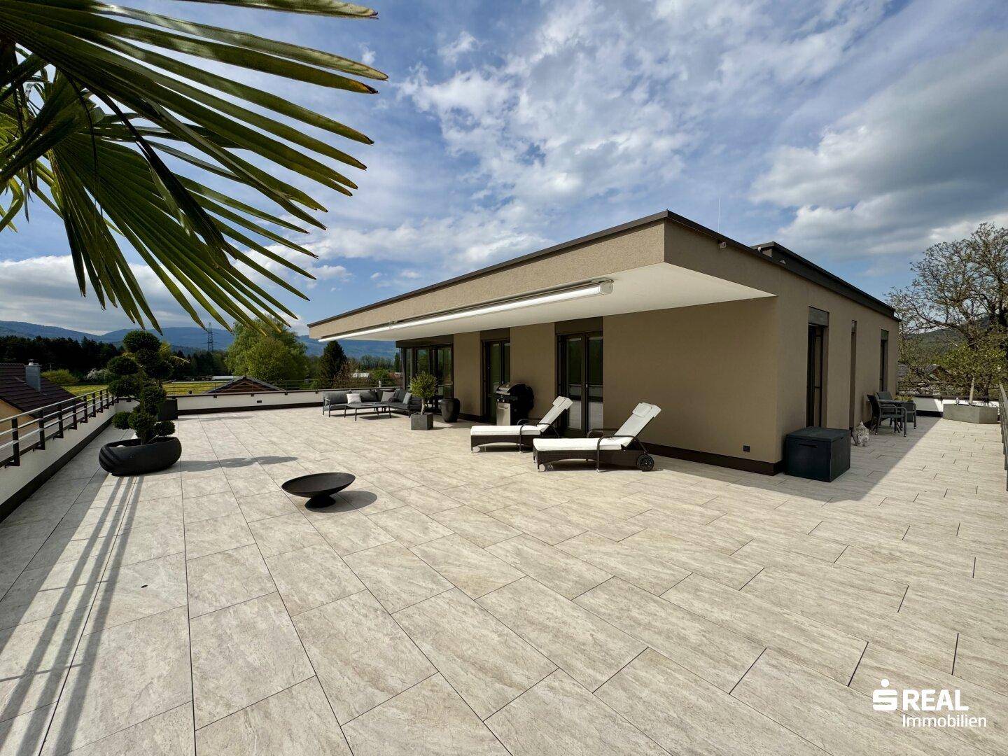 Große, sonnige Dachterrasse mit modernen Loungemöbeln, Liegestühlen und weitem Blick in die Landschaft.