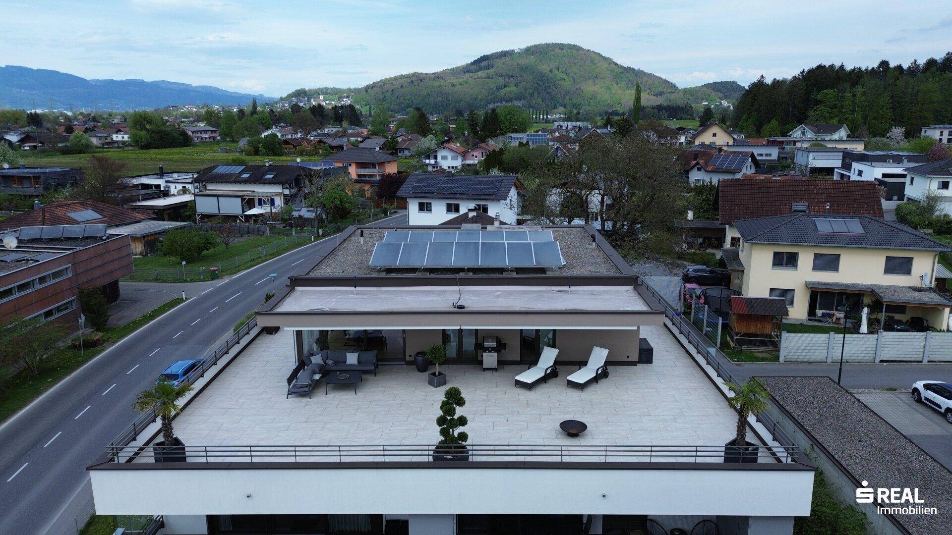 Luftaufnahme der Wohnanlage mit Dachterrasse und Blick auf die umliegende Landschaft und Berge.
