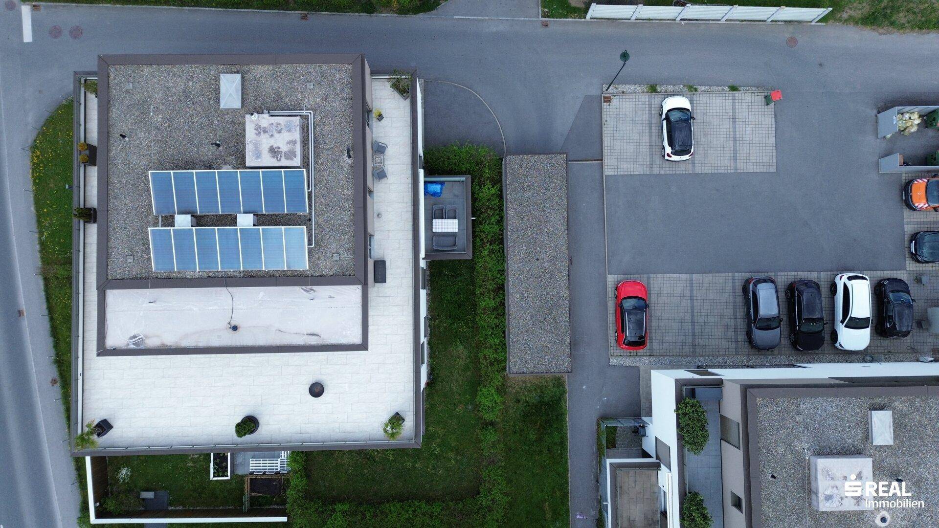 Draufsicht auf die Wohnanlage mit Dachterrasse, Photovoltaikanlage und Parkplätzen.