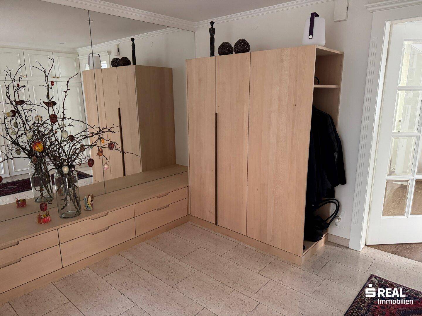 Heller Eingangsbereich mit maßgefertigten Holzschränken, großem Spiegel und hellem Fliesenboden.