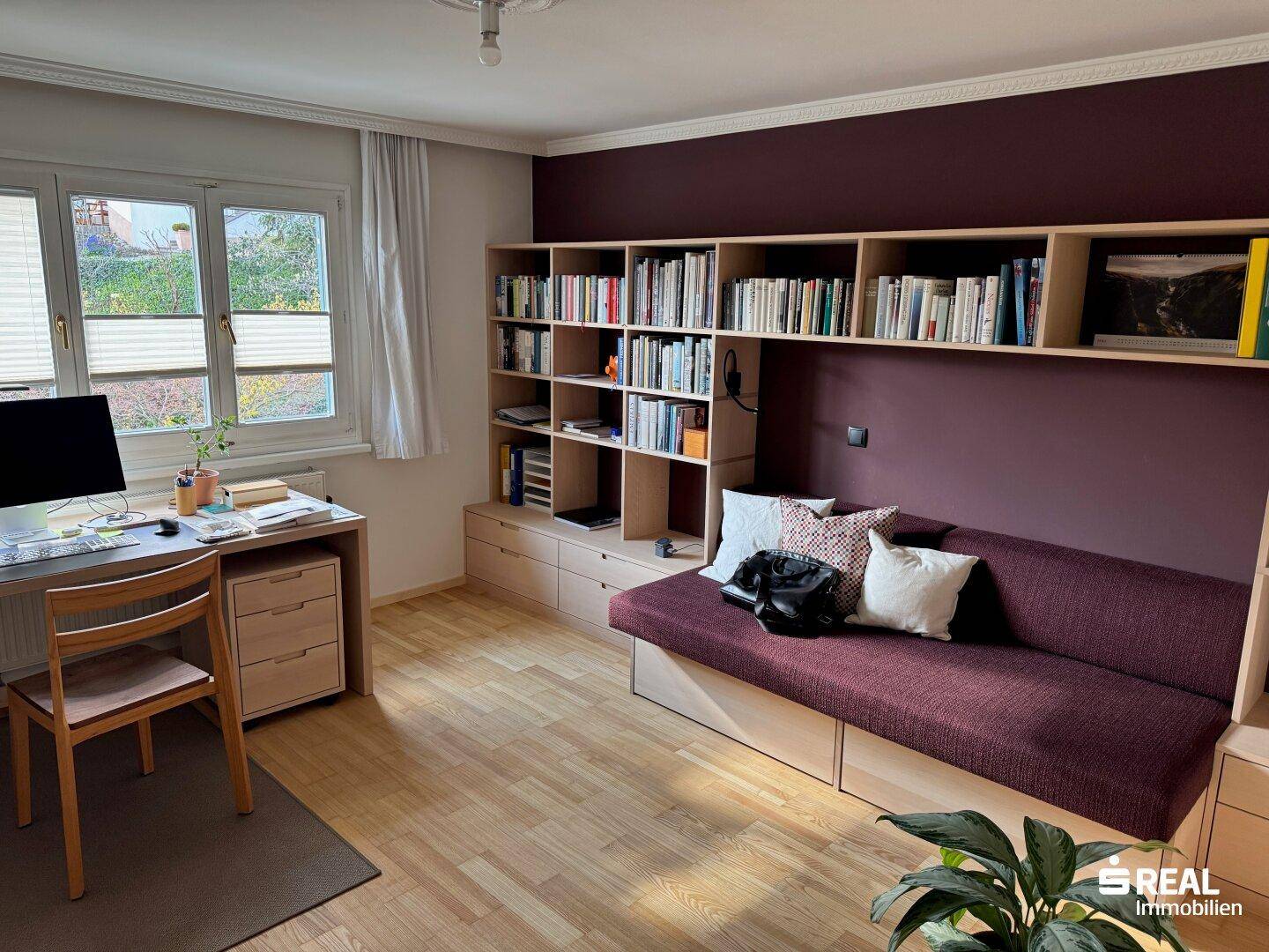 Gemütliches Arbeitszimmer mit Schreibtisch, Schlafsofa und integriertem Bücherregal an einer farbigen Wand.
