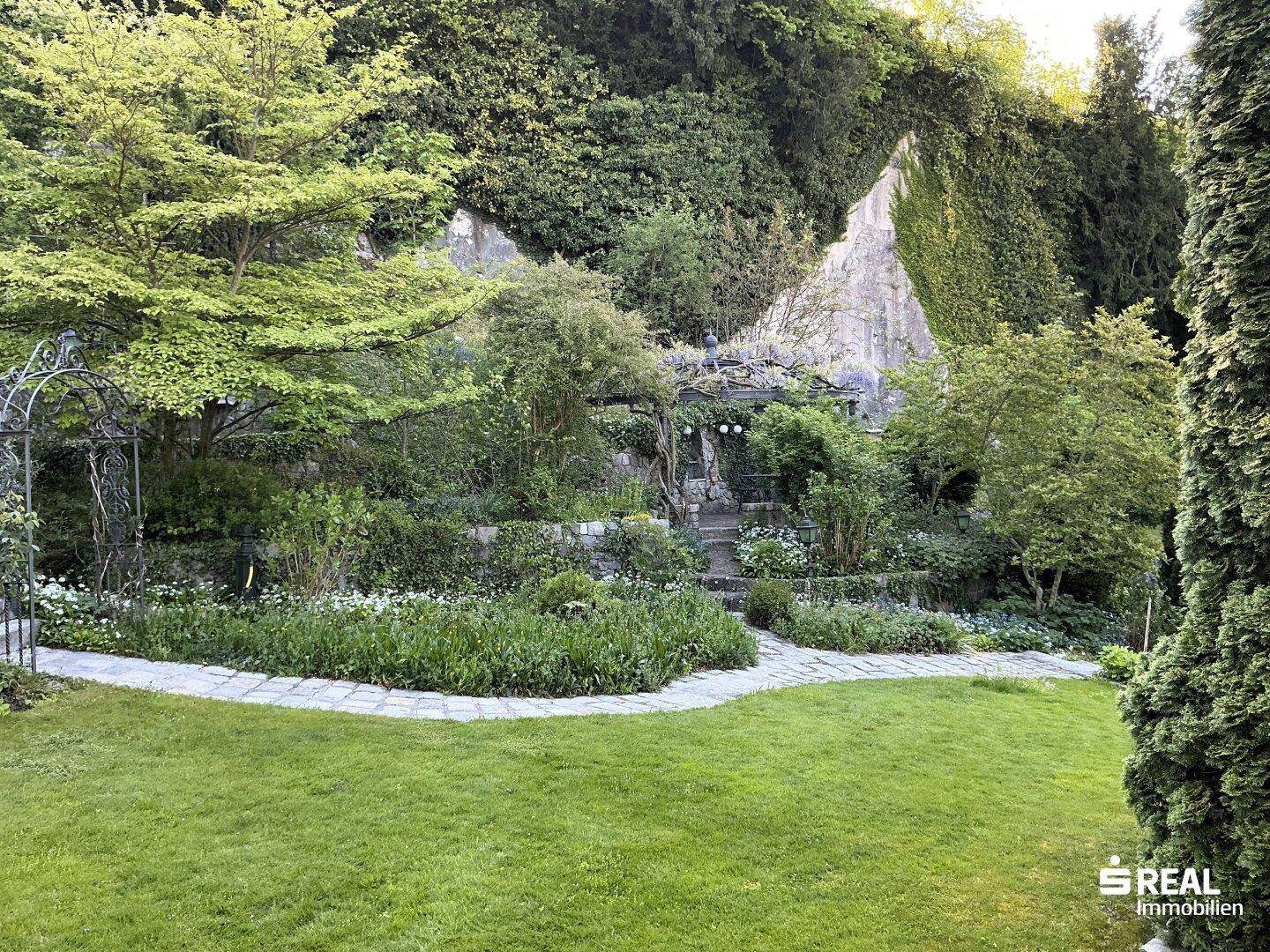 Weitläufiger, naturbelassener Garten mit alten Bäumen, Steinmauern und vielfältiger Vegetation.