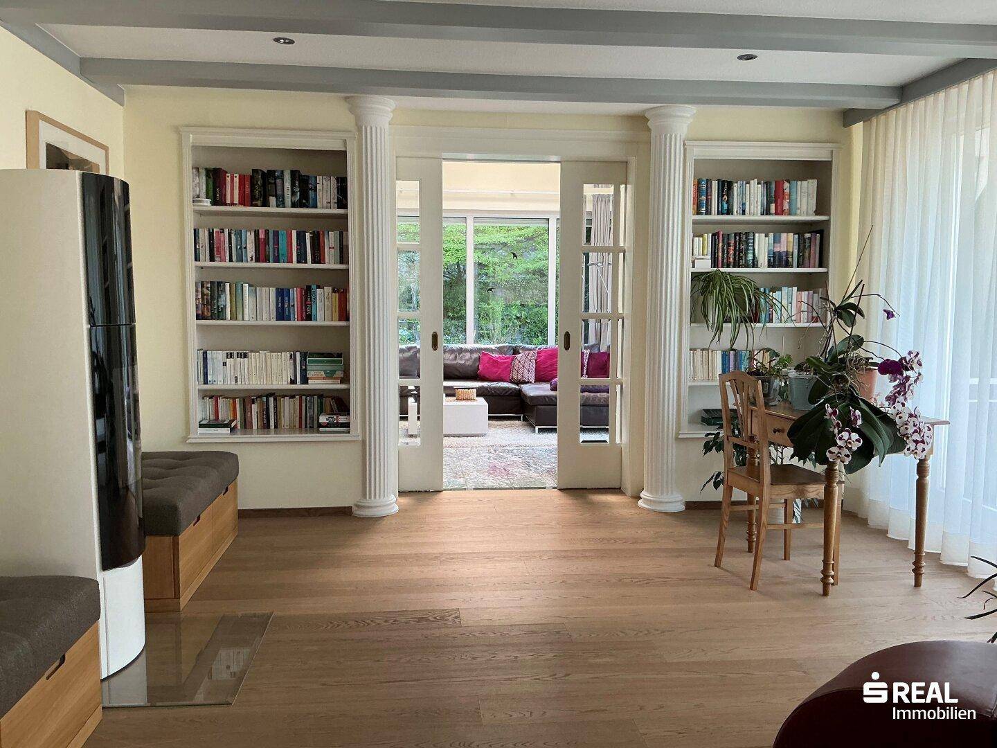 Elegantes Wohnzimmer mit eingebauten Bücherregalen, Holzboden und Doppeltüren zu einem weiteren Wohnbereich.