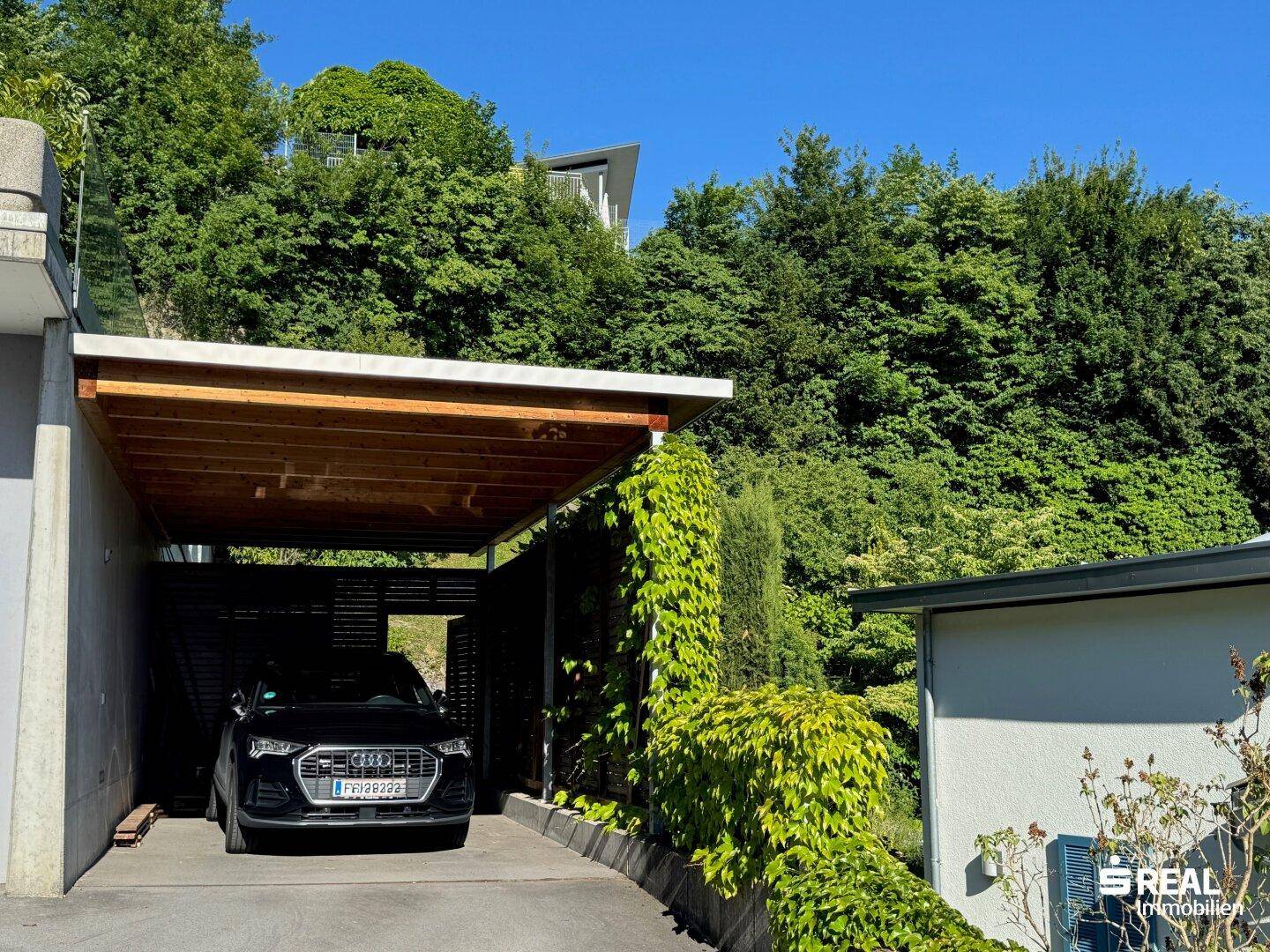 Überdachter Carport mit Holzkonstruktion und üppiger Begrünung, eingebettet in die Natur.