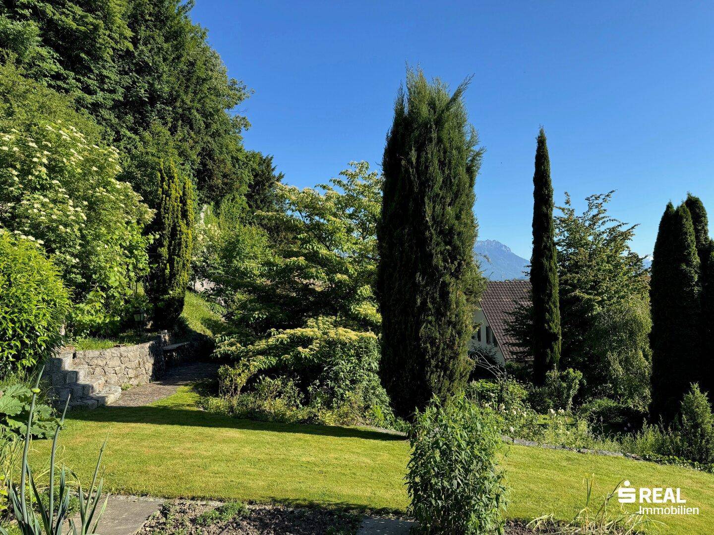 Malerischer Gartenweg mit Steinstufen, umgeben von üppigem Grün und hohen Bäumen.