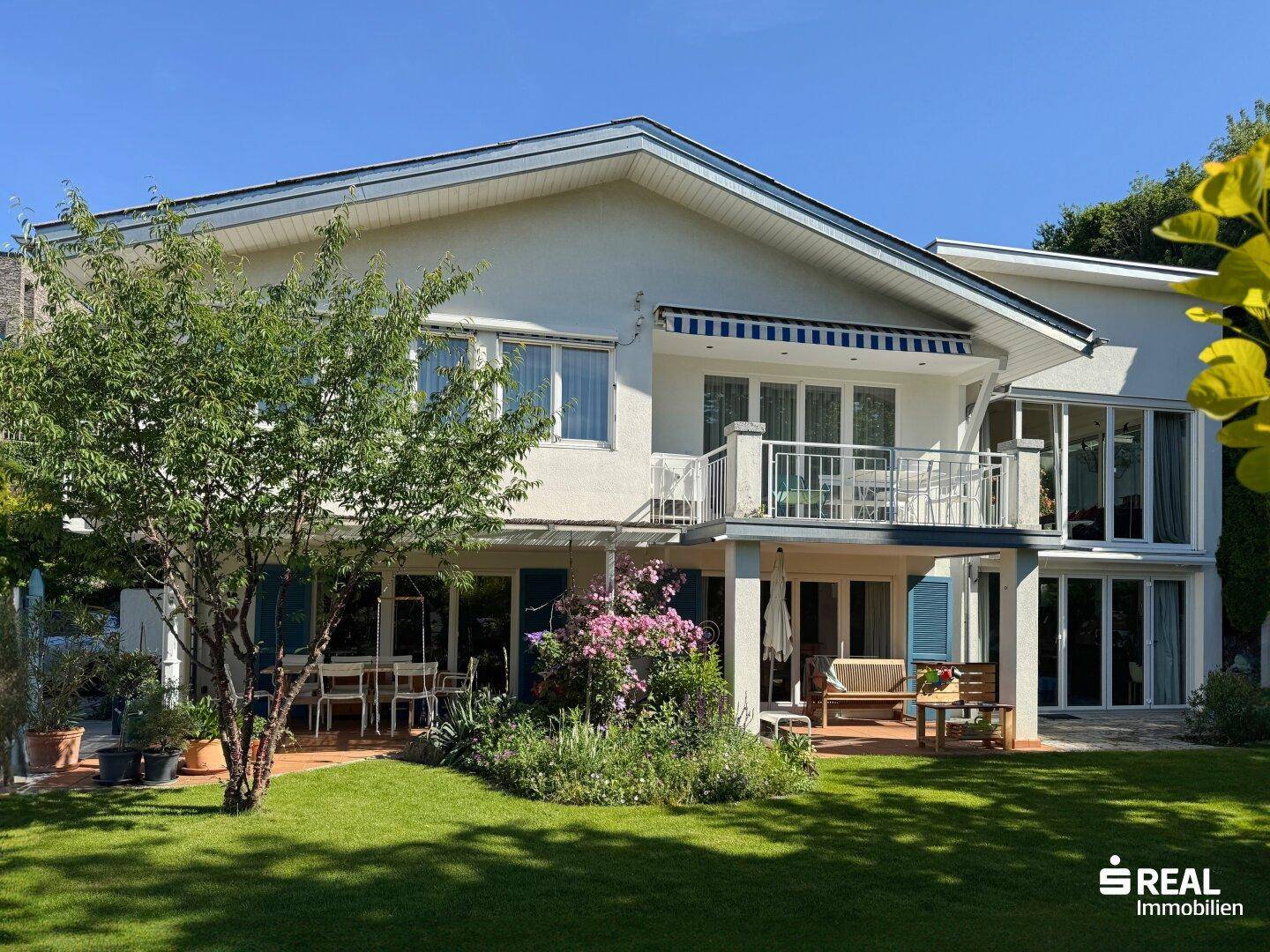 Rückseite des Hauses mit mehreren Balkonen, einer Terrasse und einem gepflegten Gartenbereich.