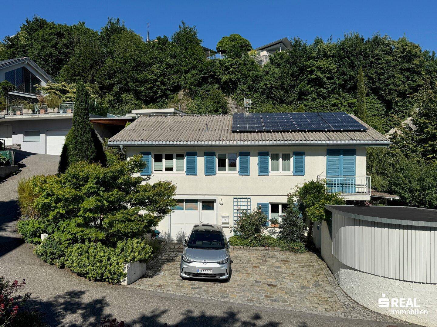 Vorderansicht des Hauses mit gepflasterter Auffahrt, Solaranlagen auf dem Dach und grüner Umgebung.