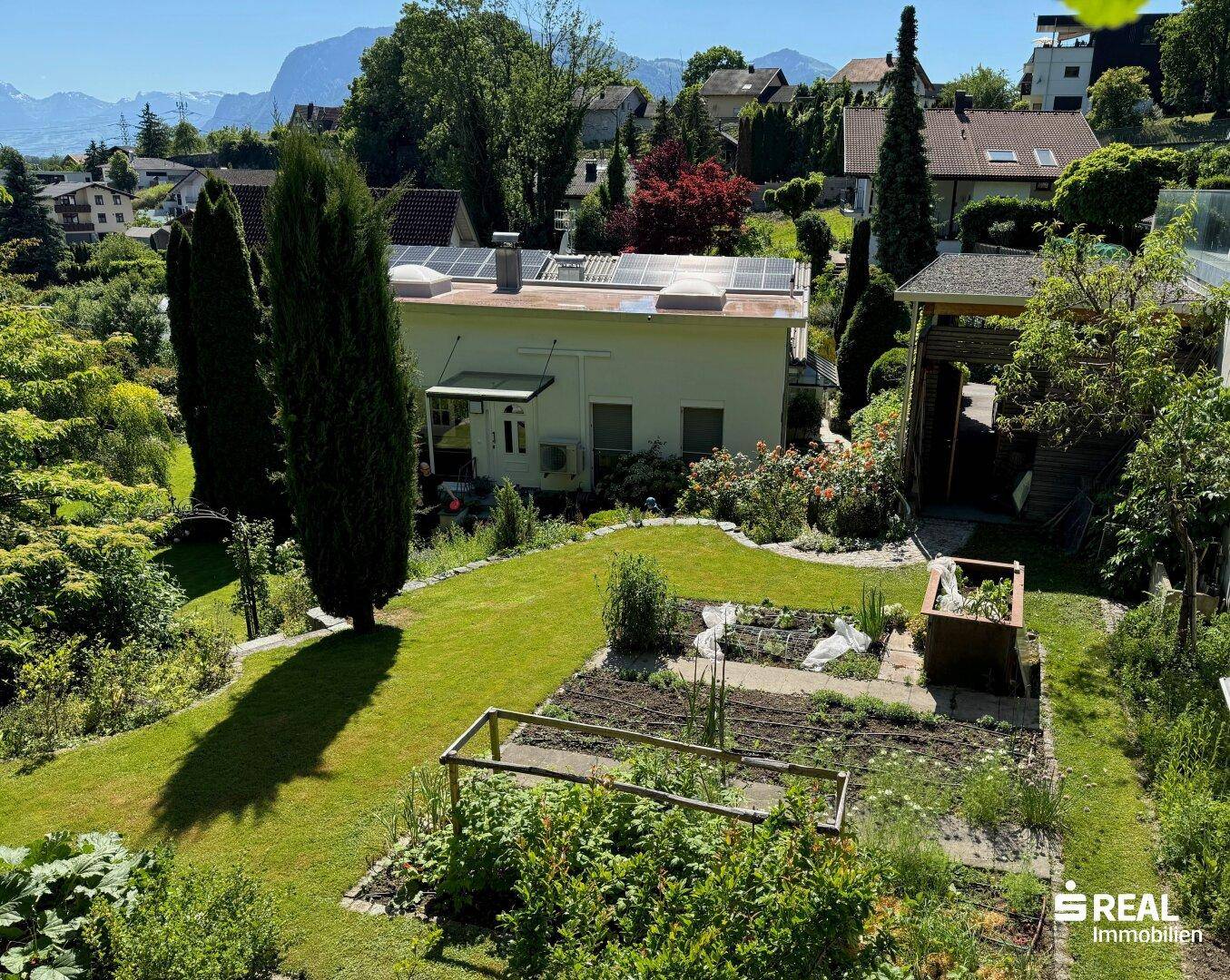 Weitläufiger Gartenbereich mit Rasen, Hochbeeten und Blick auf die umliegende Landschaft und Berge.