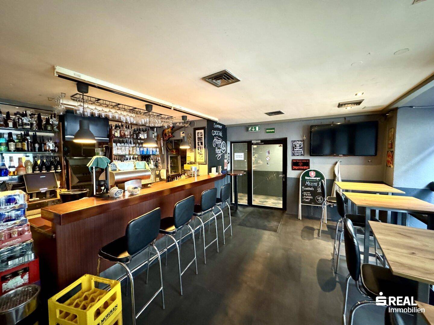 Thekenbereich einer Bar mit Flaschenregalen, Zapfanlage und Hockern, bereit für den Betrieb.