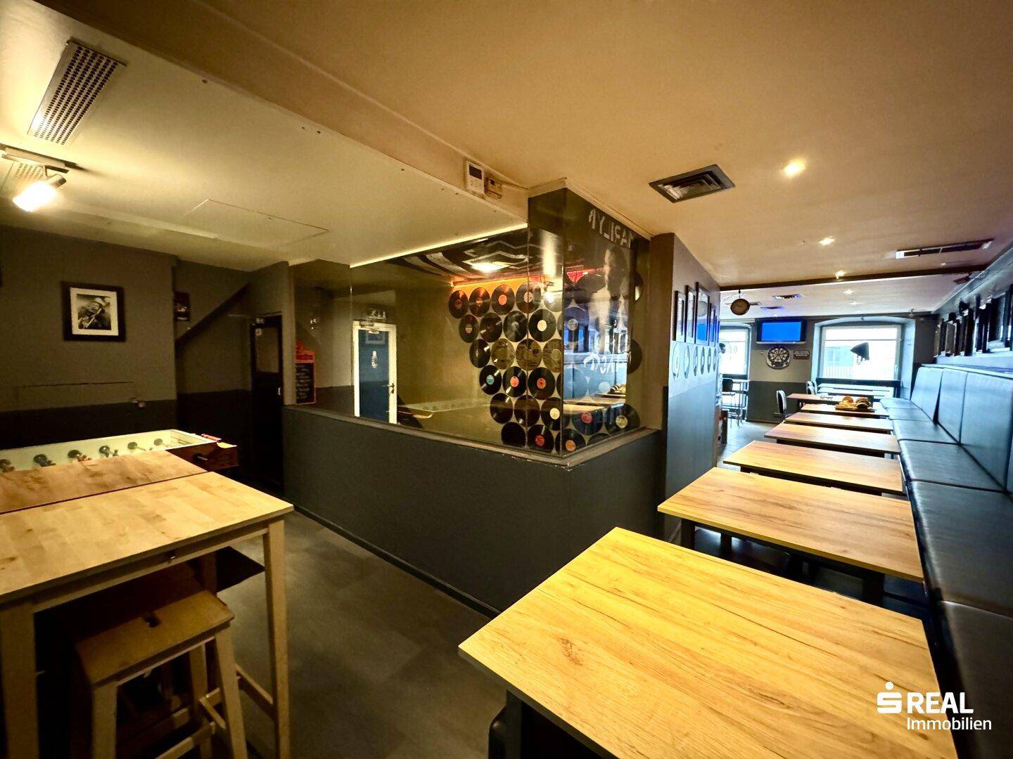 Sitzbereich einer Bar mit gepolsterten Bänken und Holztischen, dekoriert mit Schallplatten an der Wand.