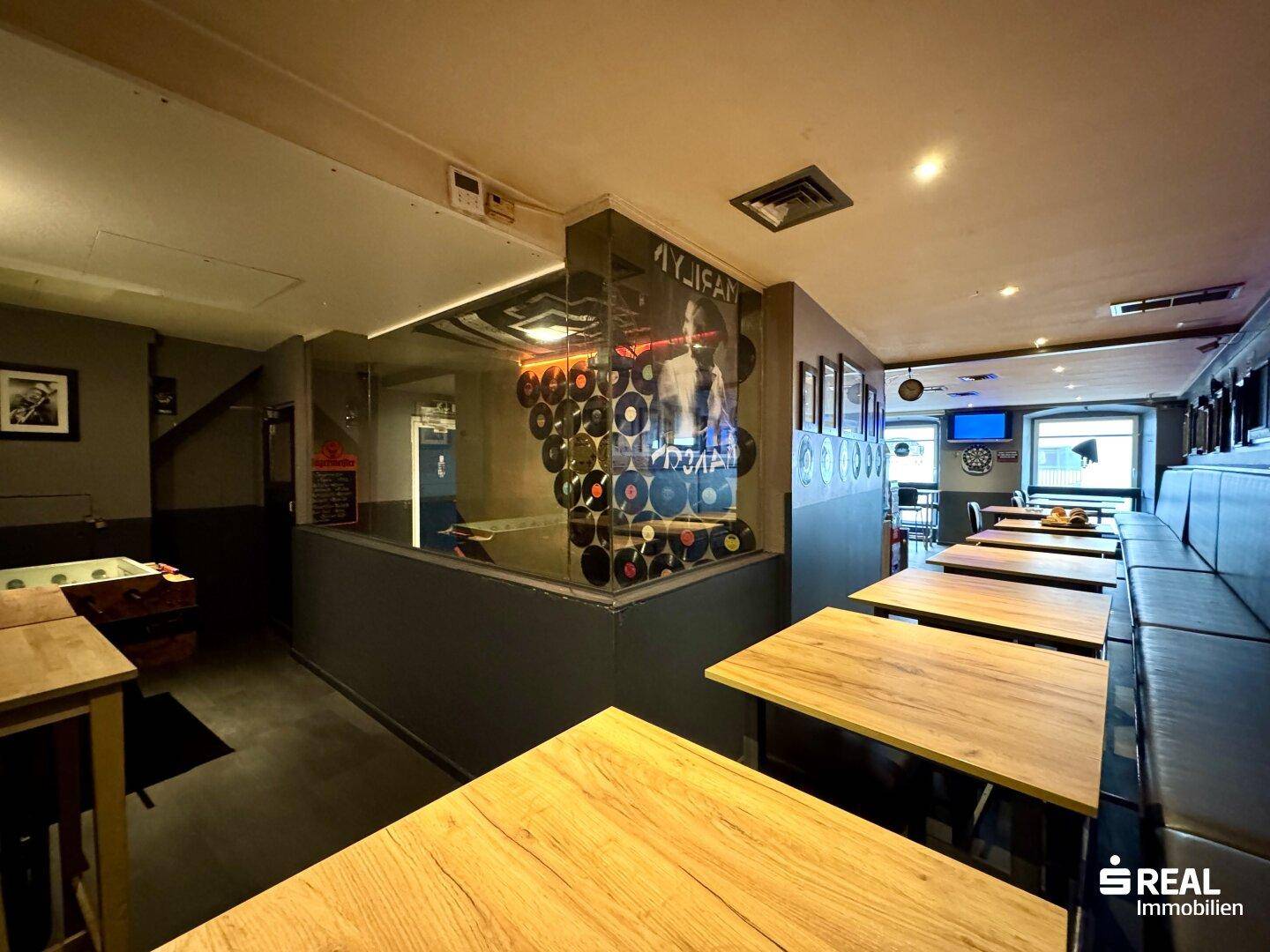 Innenansicht einer Bar mit Sitzgelegenheiten, Tischen und einer dekorativen Wand aus Schallplatten.