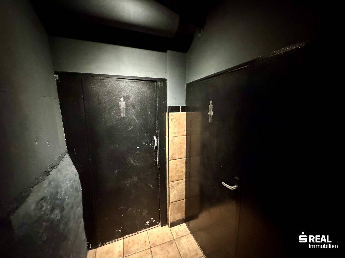 Eingang zu den Toiletten mit getrennten Türen für Damen und Herren, dunkle Beleuchtung.
