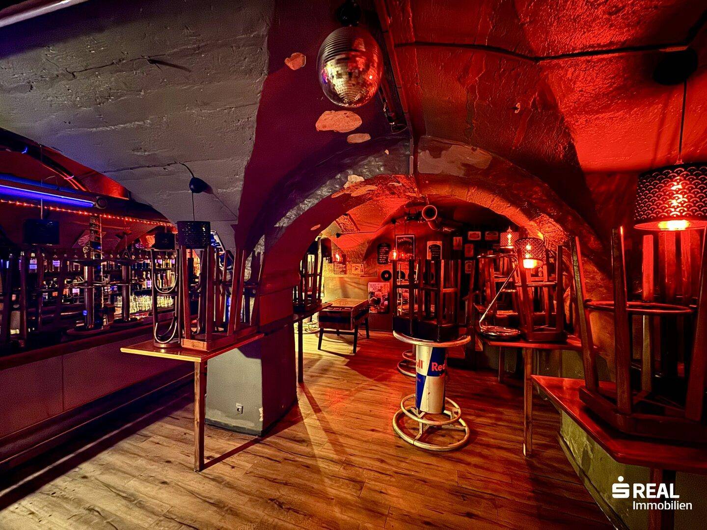 Kellerbar mit roter Beleuchtung, Spiegelkugel und rustikalen Möbeln, einladende Atmosphäre.