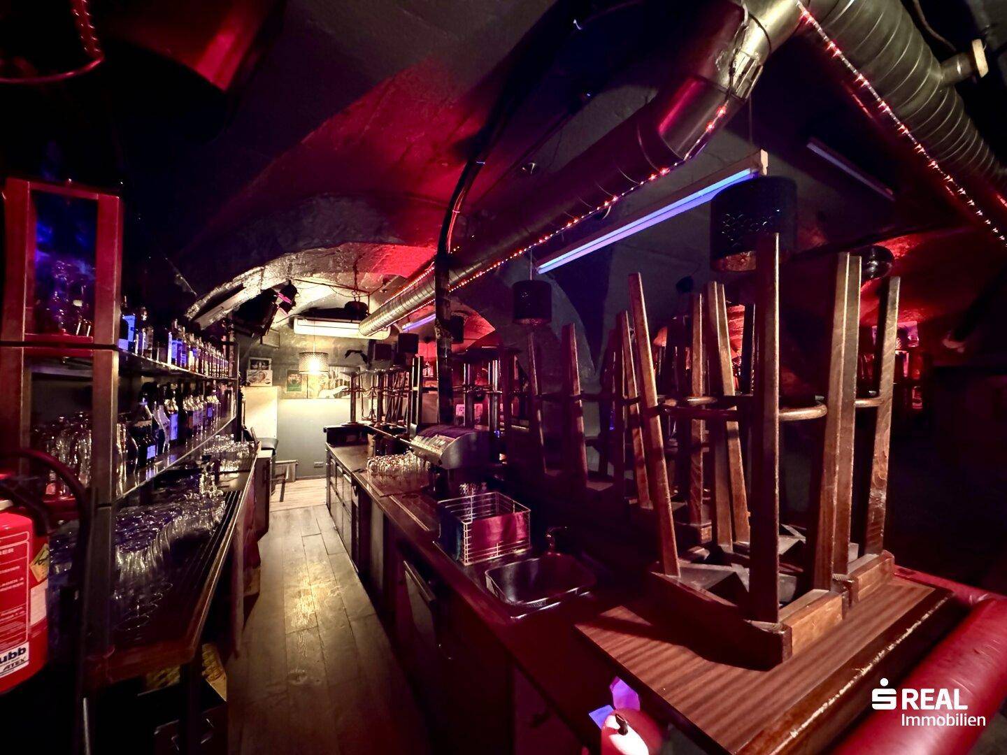 Bartheke in einer Kellerbar mit roter Beleuchtung und vielen Gläsern, gut ausgestattet.