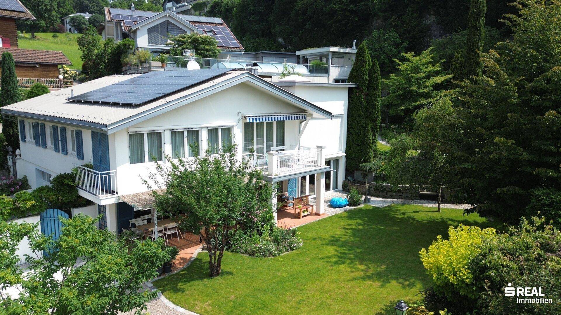 Großzügiges Einfamilienhaus mit weitläufigem Garten, mehreren Terrassen und Photovoltaikanlage auf dem Dach.