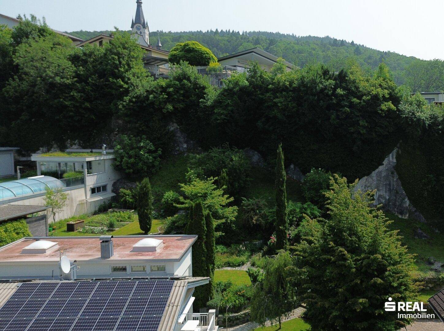 Blick auf die grüne Hügellandschaft und die umliegenden Häuser mit einem Kirchturm im Hintergrund.