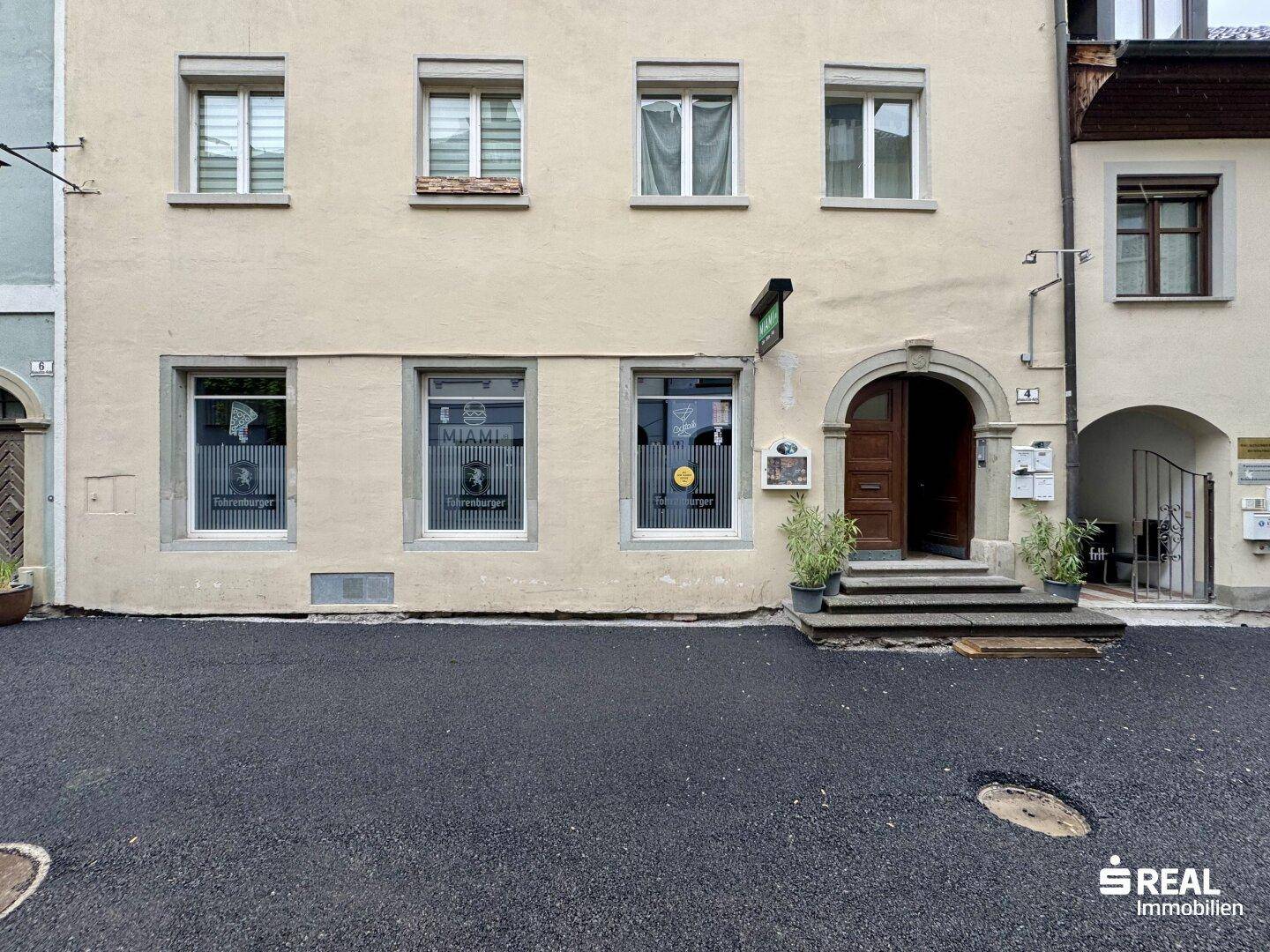Fassade eines historischen Gebäudes mit großen Fenstern und einem bogenförmigen Eingangsbereich.